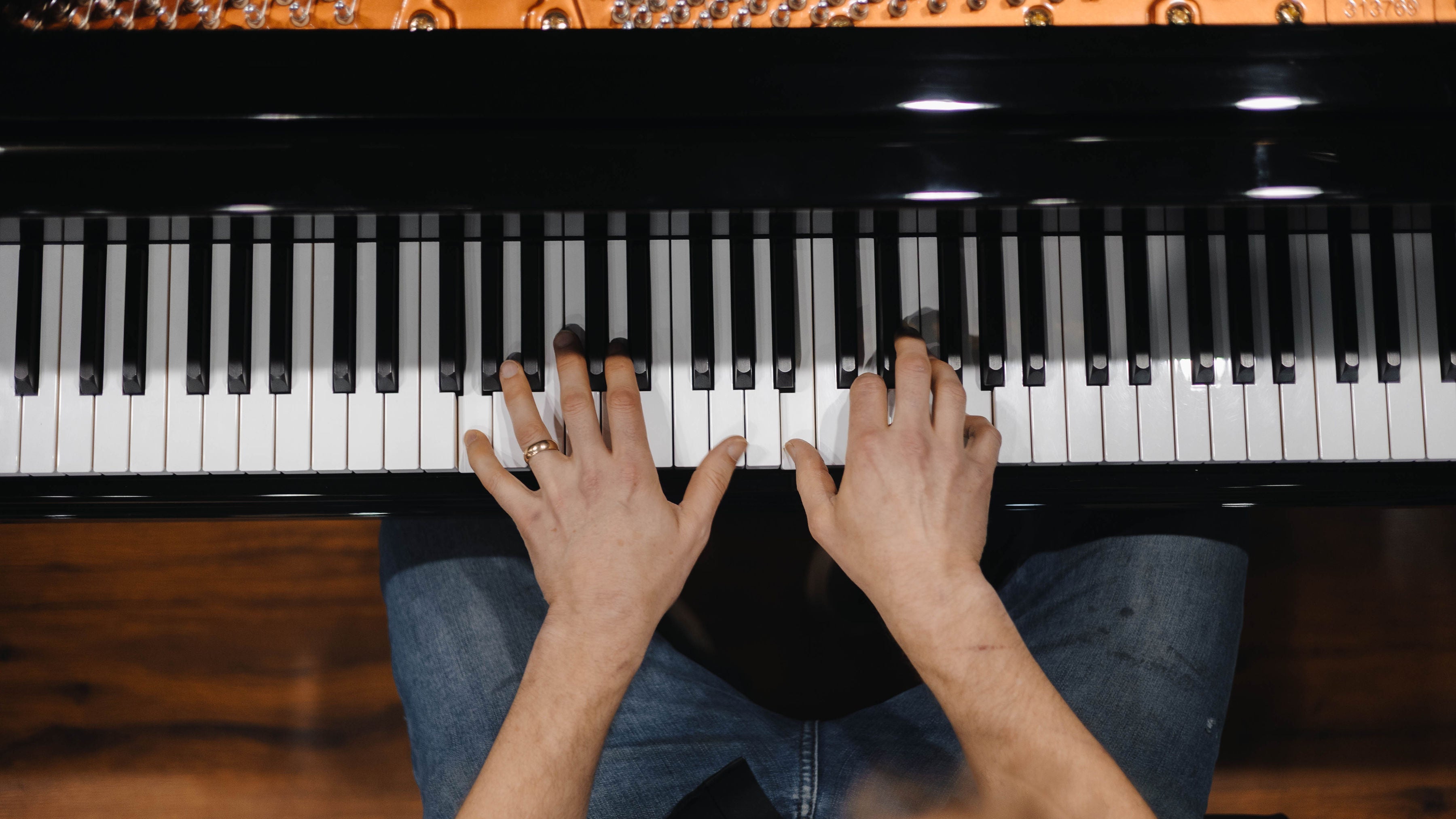Brigham Larson sitting on a piano bench with his hands on the piano keys, playing a Hailun Grand piano in the piano sales showroom at Brigham Larson Pianos in Orem, UT.