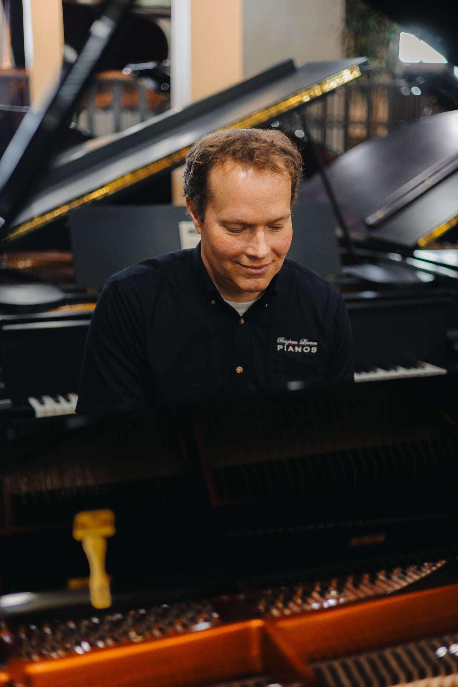 Brigham Larson playing a polished black Hailun Grand Piano in the piano sales showroom floor with lined up grand and upright pianos in rows at Brigham Larson Pianos in Orem UT.