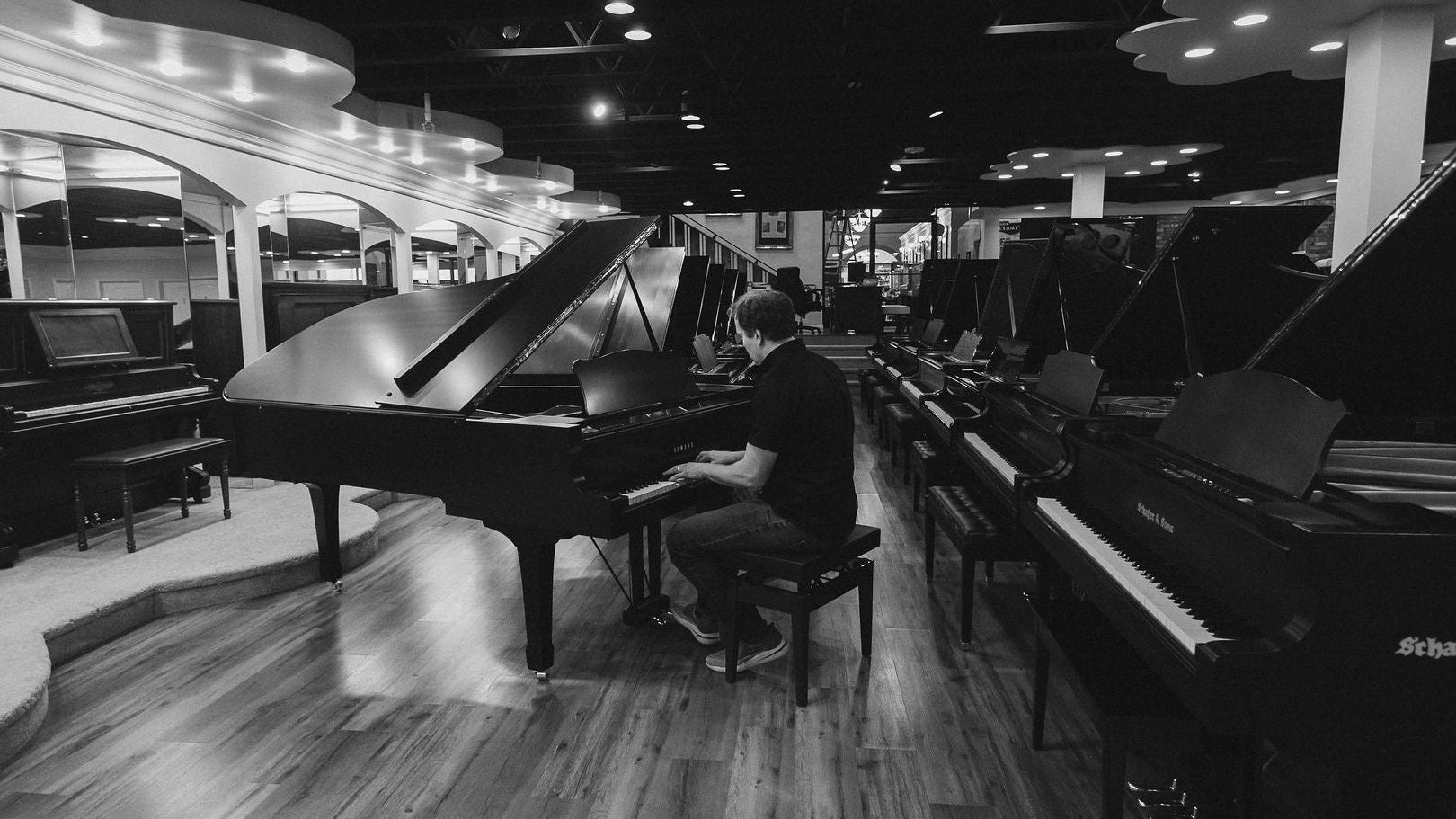Brigham Larson sitting at a grand piano playing a piano in a showroom with other pianos on display at Brigham Larson Pianos showroom in Orem, Utah.