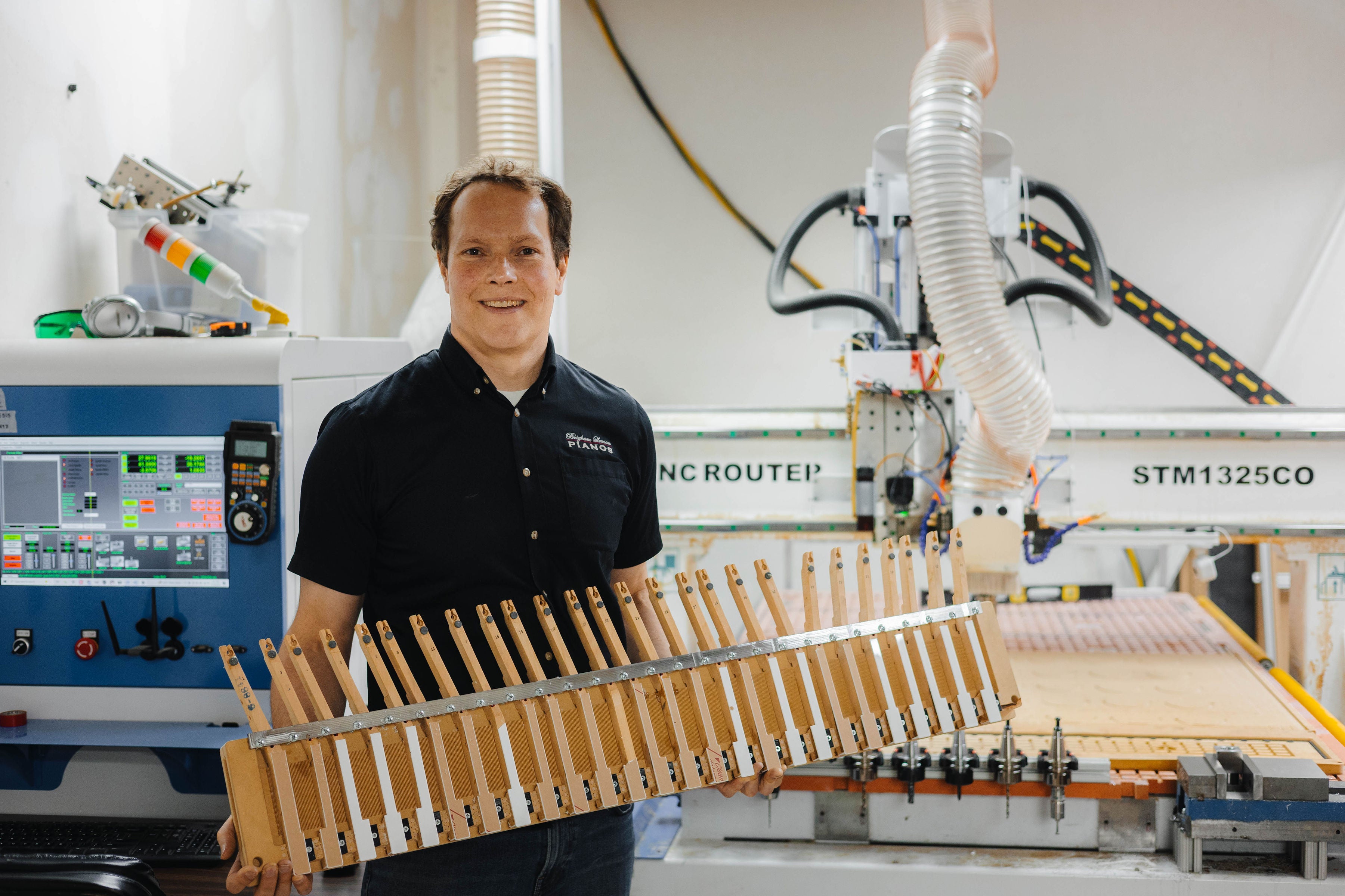Brigham Larson holding a wooden product in front of a CNC router machine at Brigham Larson Pianos Orem Utah family heirloom piano restoration shop.