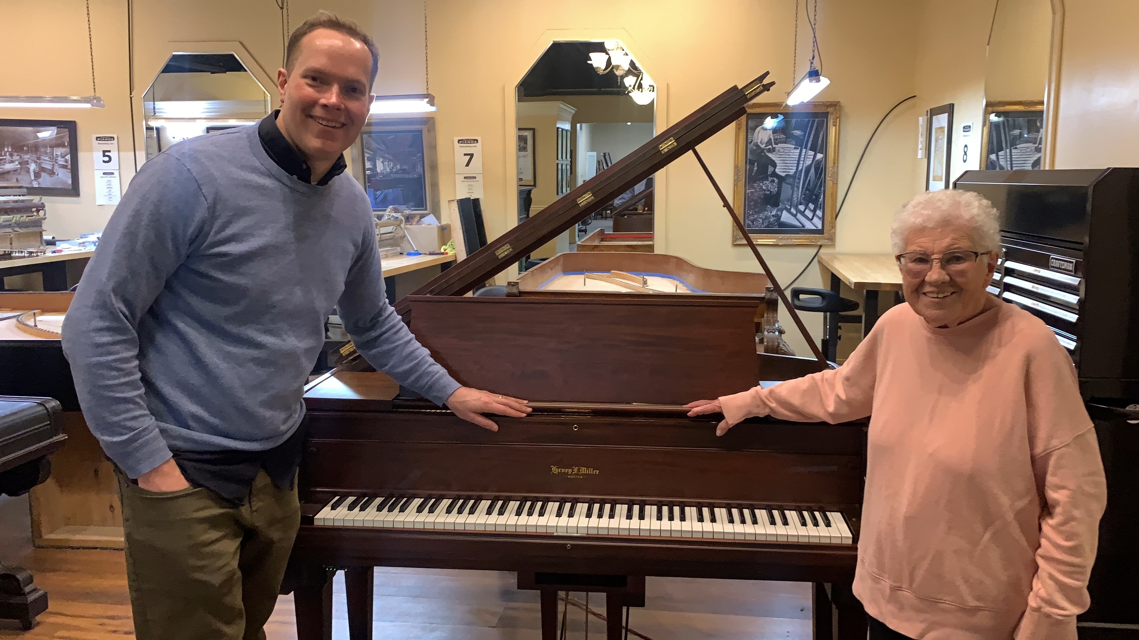 Load video: Brigham with happy customer and her restored sentimental grand piano. Beautifully restored and refinished grand Henry F Miller heirloom piano in Brigham Larson Pianos family heirloom restoration shop.