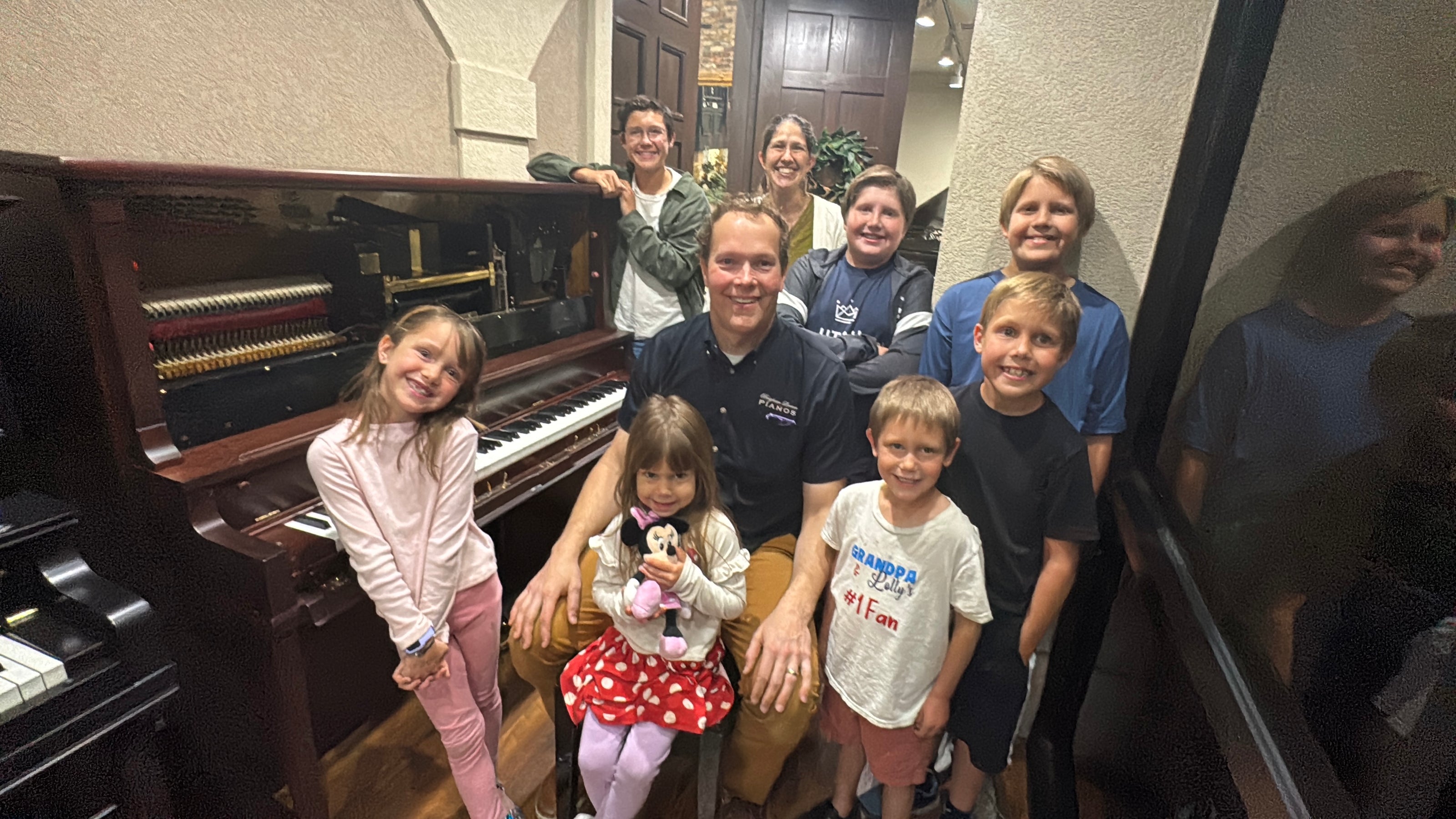 Family posing in front of a piano at Brigham Larson Pianos, seeing their fully restored Gulbransen upright piano for the first time. 