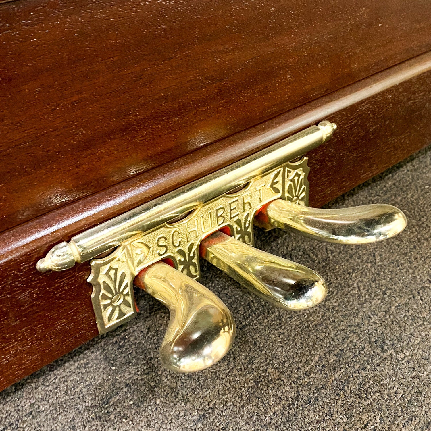 Close up of beautifully re-plated Schubert upright piano brass piano pedals after pedal restoration and brass hardware replating. Fully restored and rebuilt and refinished to like new condition at Brigham Larson Pianos family heirloom piano restoration shop in Orem, UT.