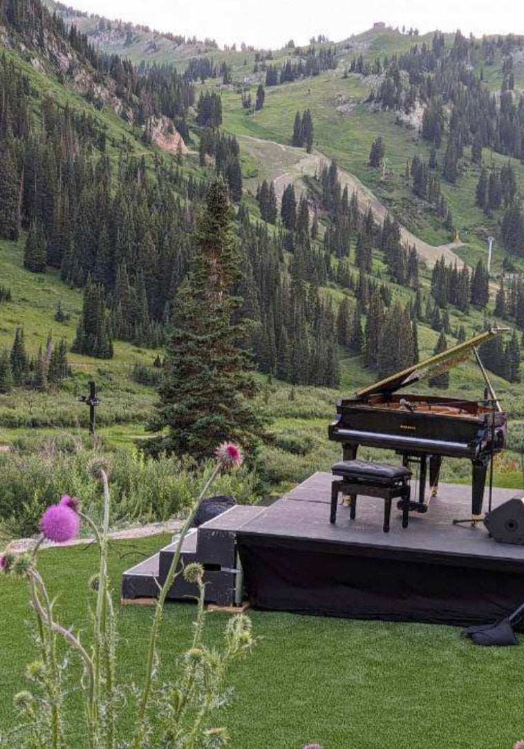 Gorgeous polished black Baldwin Grand piano on a stage with a scenic mountain backdrop for professional piano event rental in Utah.