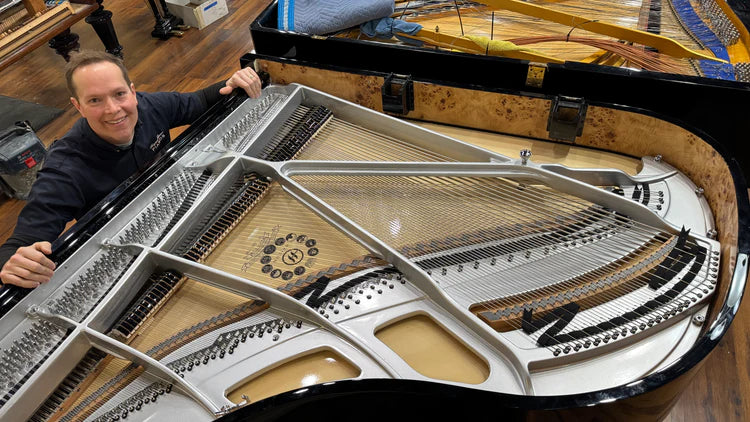 Brigham Larson  working on a Hailun 178 grand piano with the lid open, revealing the interior strings and mechanics inside of the Brigham Larson Pianos family heirloom piano restoration shop in Orem, Utah, Utah County. Hailun 178 Custom Plate & Strings—One-of-a-Kind!
