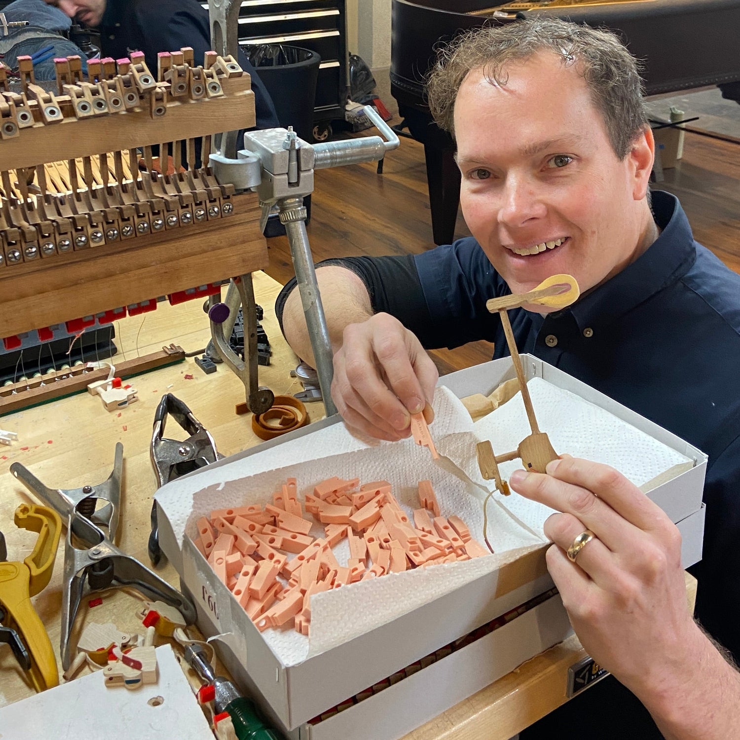 Brigham Larson holding a 3D printed piano action part at the Brigham Larson Pianos in Orem, Utah piano heirloom piano restoration shop.
