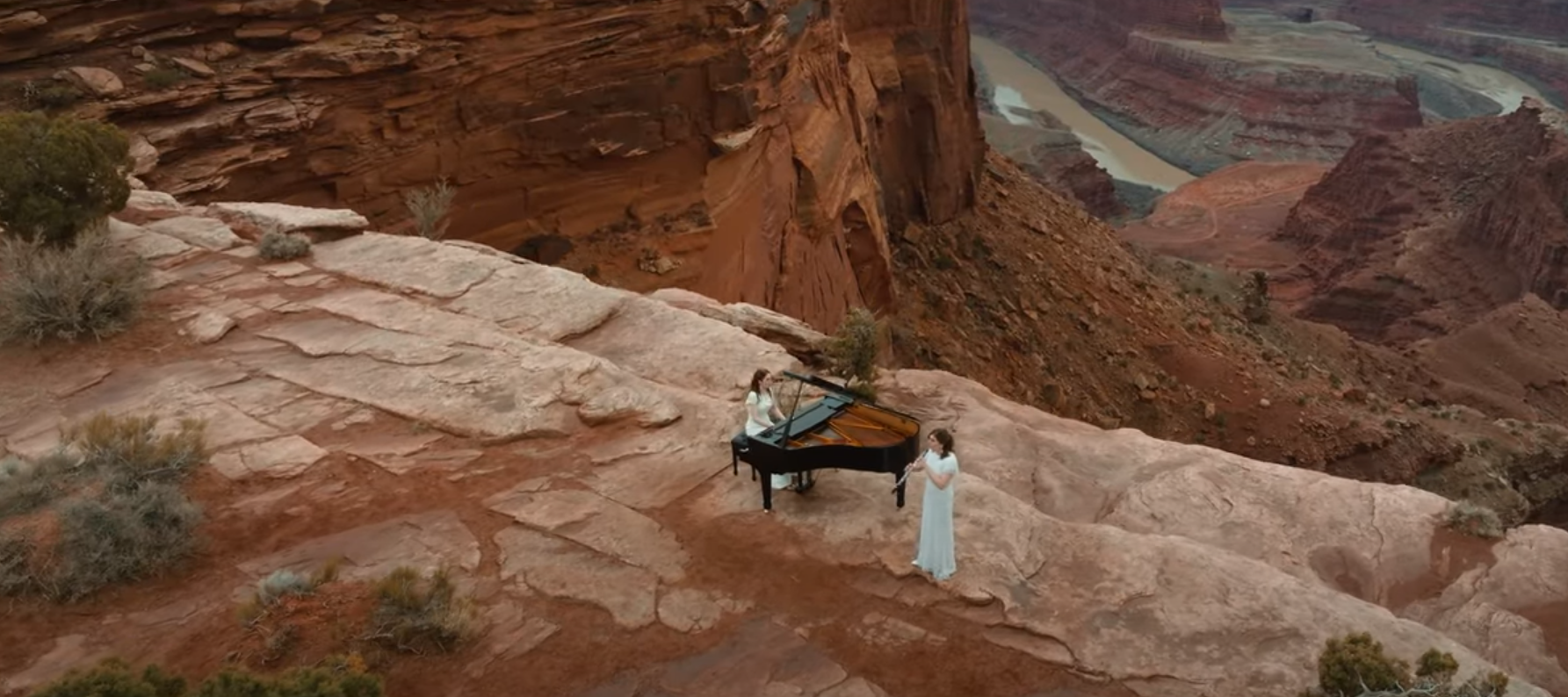 Two women playing a piano and singing on a rocky outcrop with a canyonlands background professional piano event rental in Utah. Yes, our piano movers delivered a piano rental to the top of a mountain!