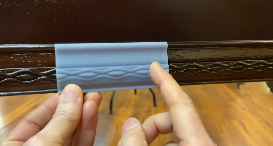 Brigham Larson holding a replicated 3D printed piano trim piece to match the missing trim on a gand Hallet Davis piano  at Brigham Larson Pianos in Orem, Utah piano heirloom piano restoration shop.