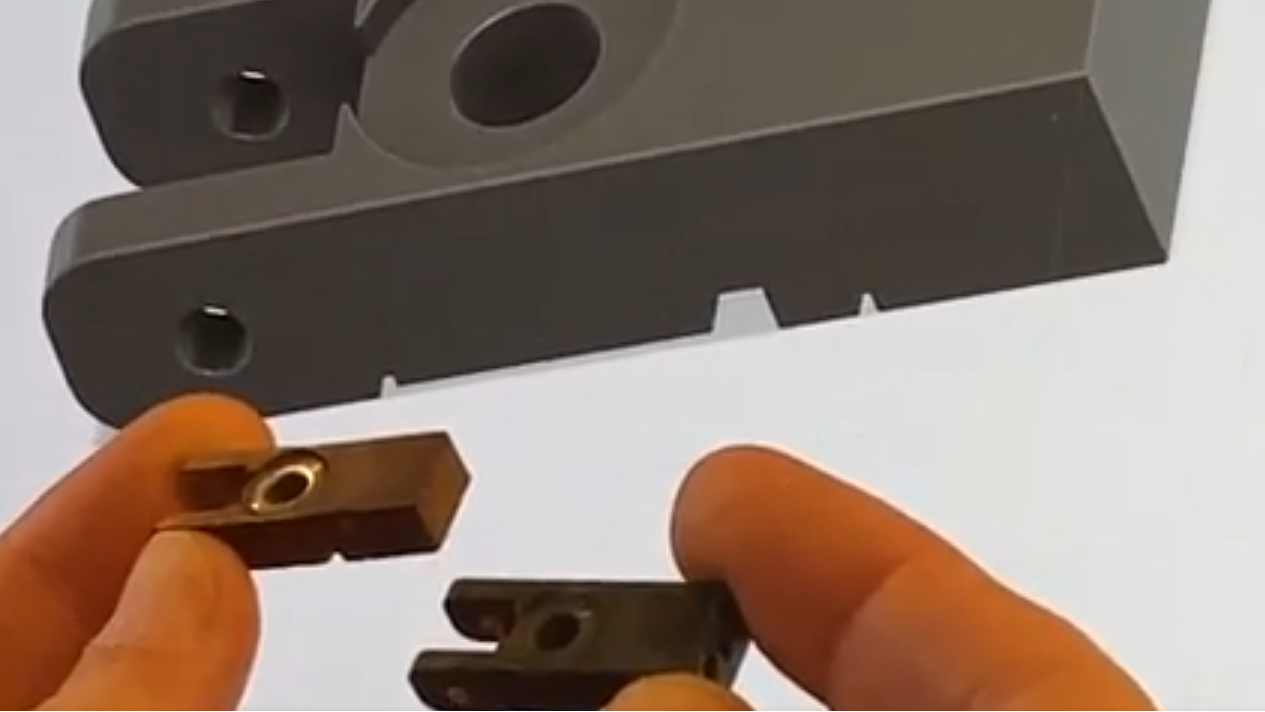 Close-up of hands holding a small piano component against a computer image of CAD component design 3D printing piano flange at Brigham Larson Pianos in Orem, Utah piano restoration shop.