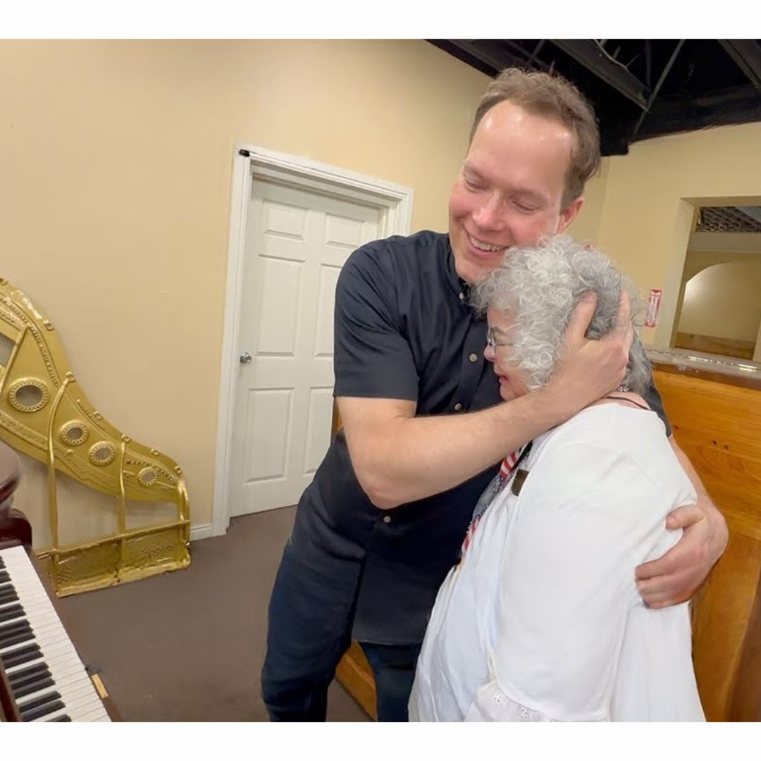 Sentimental photo of Brigham Larson registered piano technician unveiling an heirloom upright piano fully restored and refinished with modern QRS piano player system installed, to happy family who is tearful and emotional about the wonderful restoration for generations to come to enjoy in the Brigham Larson Pianos family heirloom piano restoration shop in Orem, UT.