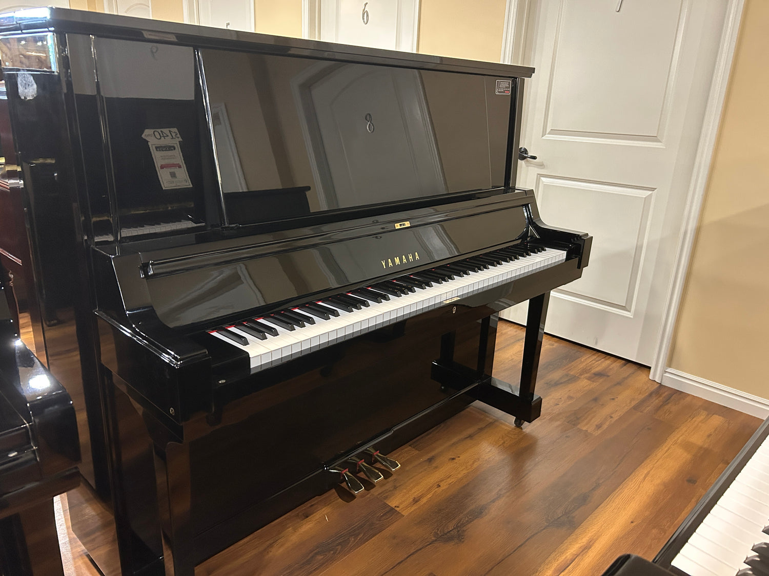 Polished Black Yamaha YUA upright piano in a showroom piano sales floor with wooden floor and white walls.