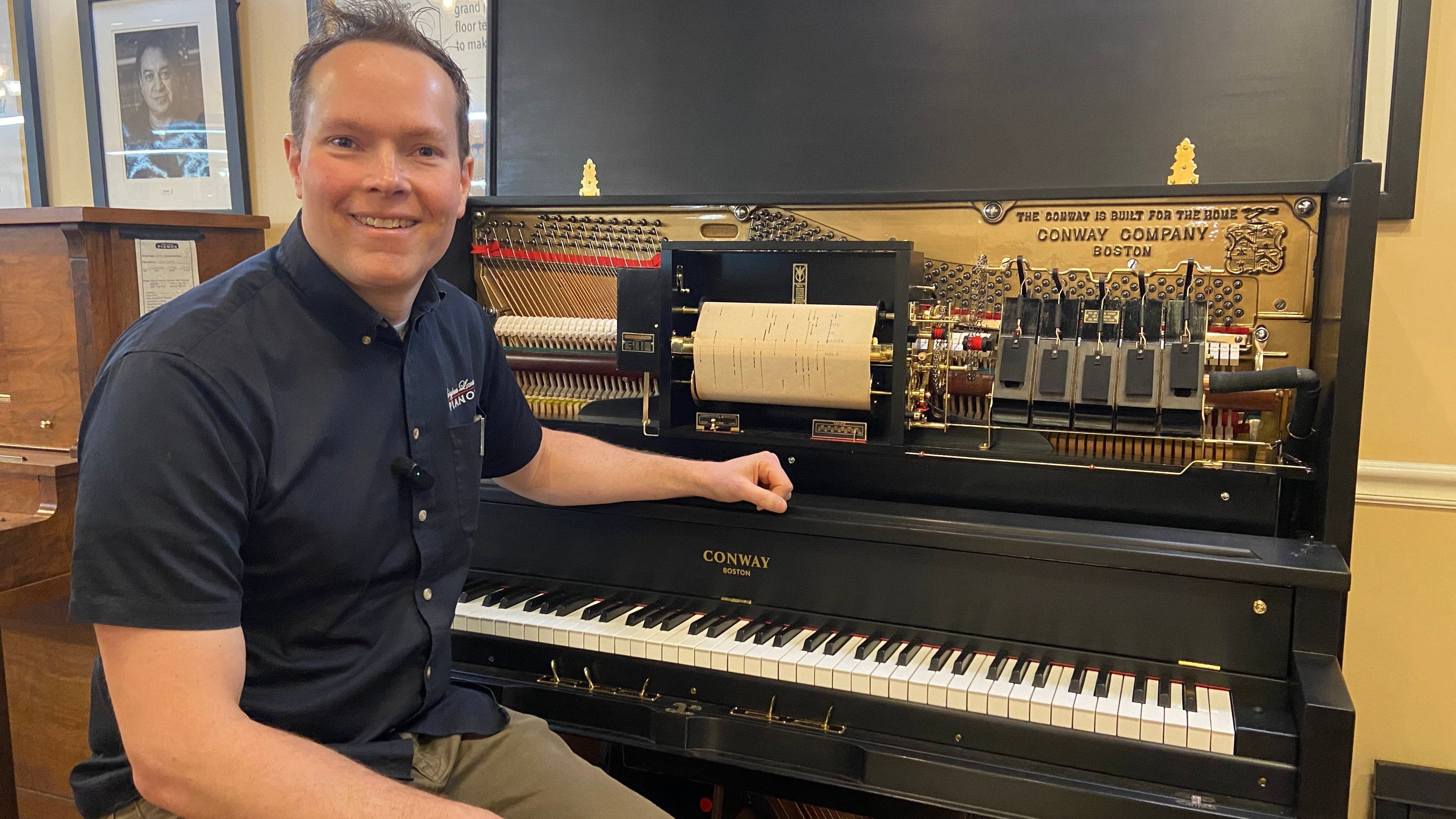 Brigham Larson sitting by fully rebuilt 1923 Conway upright player piano at Brigham Larson Pianos, in Orem, UT.