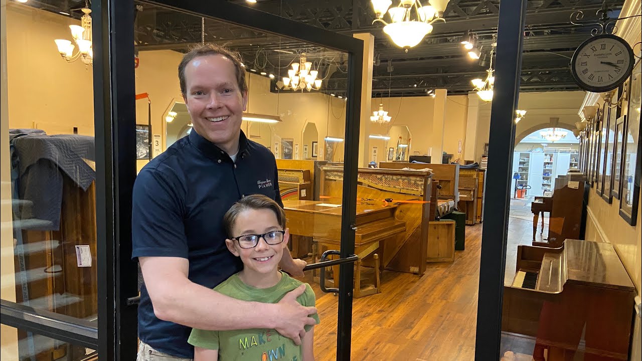 Brigham Larson and son standing inside a store going on a piano restoration shop tour, with family heirloom piano restoration shop at Brigham Larson Pianos in Orem, UT.