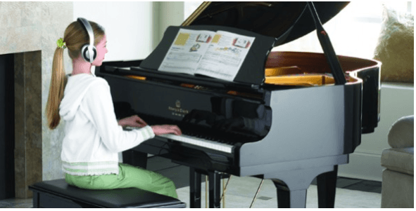 Young woman at a grand piano with headphones on playing the digital grand player piano silent play system.